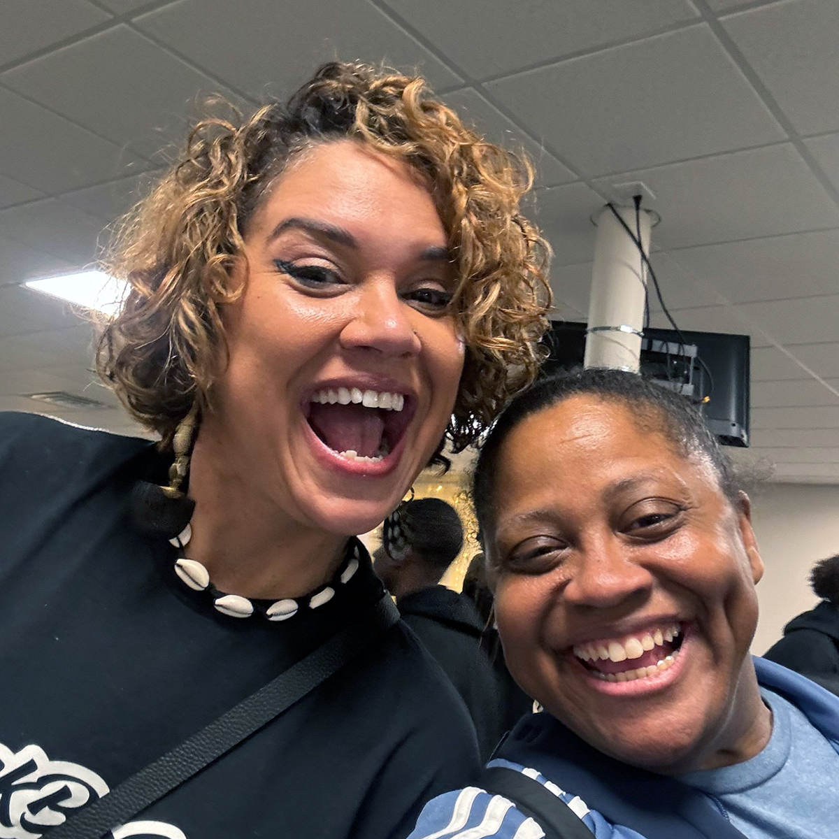 Crystal Good shares a joyful moment at Black Policy Day. Good is wearing a black top with cowrie shell necklace and the other is dressed in navy, both with genuine smiles in this casual selfie.