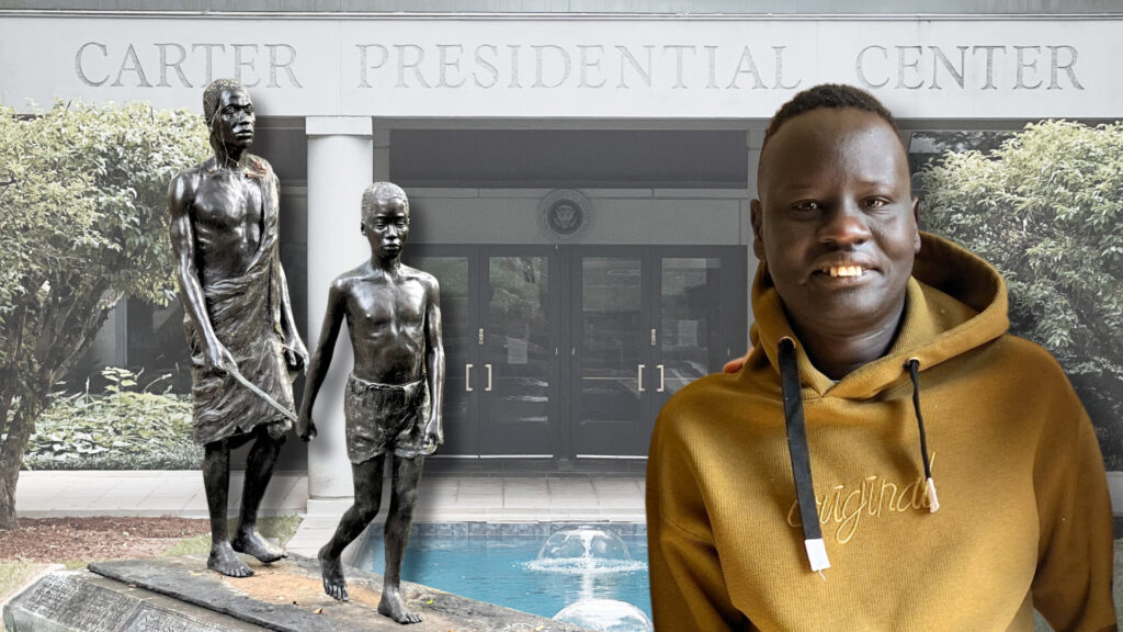 A South Sudanese refugee wearing a yellow hoodie smiles at the camera while standing in front of the Carter Presidential Center entrance. Behind him are two bronze statues depicting African figures, and a small fountain is visible in the background. The Center’s name is prominently displayed in large letters above the entrance.