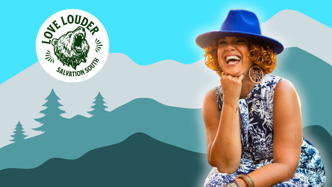 Affrilachian poet Crystal Good, founder of Black by God West Virginia, laughs joyfully wearing a bright blue hat and floral dress against an Appalachian mountain backdrop, embodying her mission to amplify Black journalism in West Virginia.