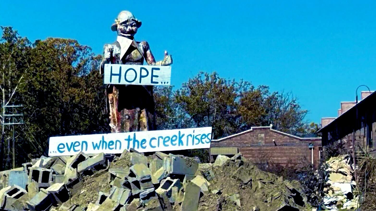 A statue in Asheville's River Arts District holding signs reading "HOPE... even when the creek rises," symbolizing resilience and hope after Hurricane Helene's impact.